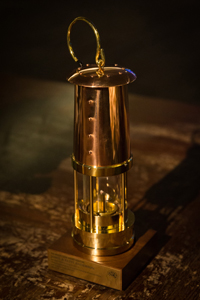 A brass miner's lamp sits on a wood table
